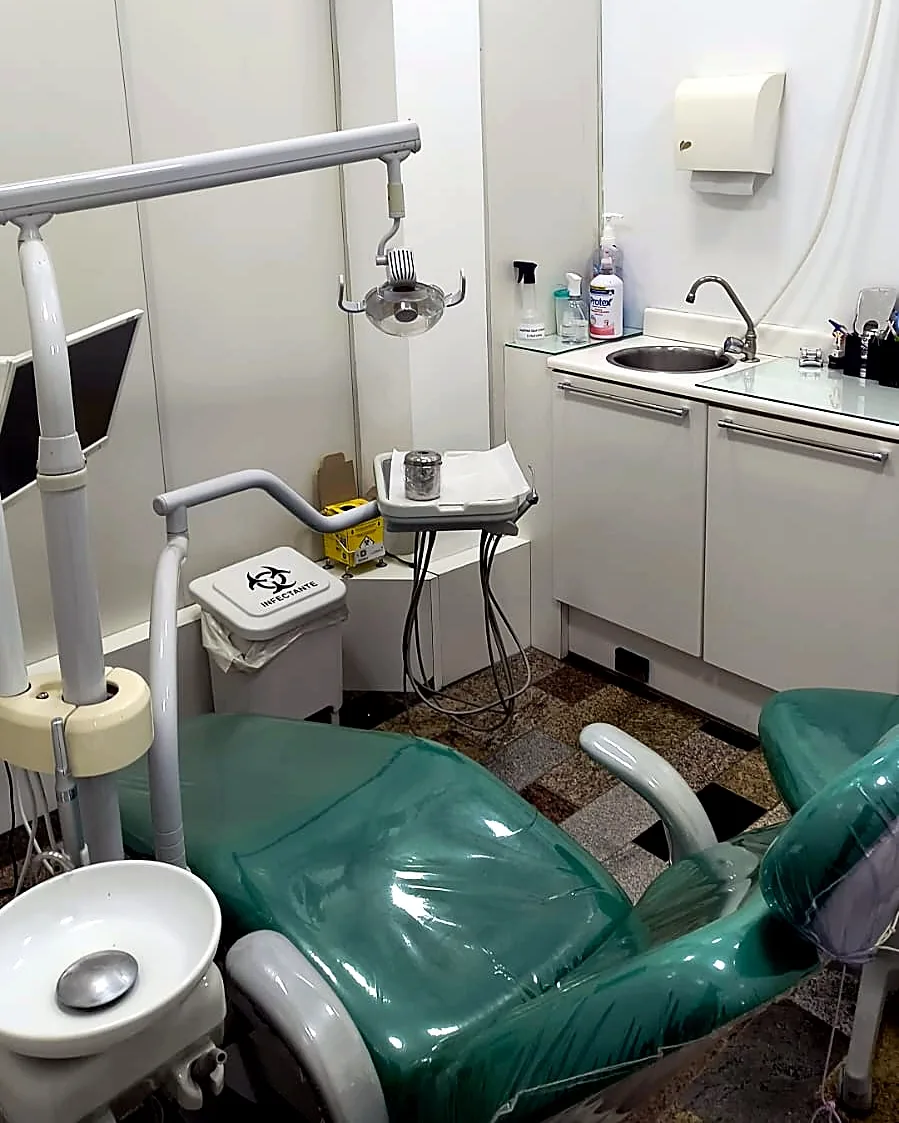 Sala de atendimento do consultório, com cadeira odontológica, refletor e bancada de instrumentos